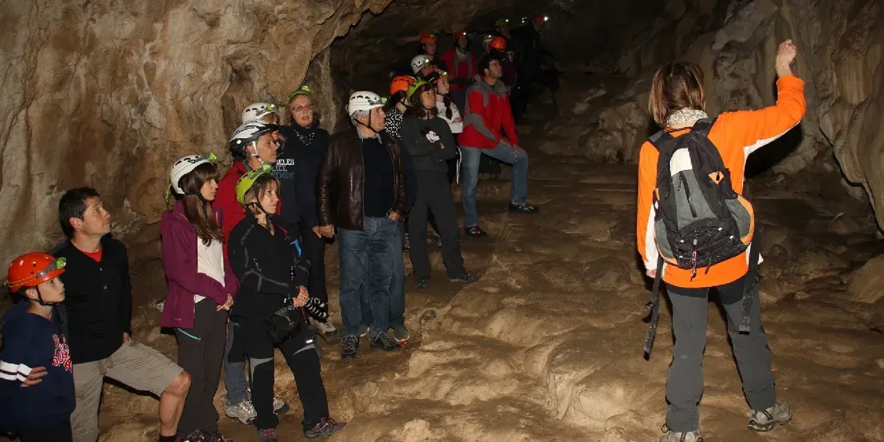 Grupo de exploradores con cascos y linternas en la cueva del oso, observando formaciones rocosas.