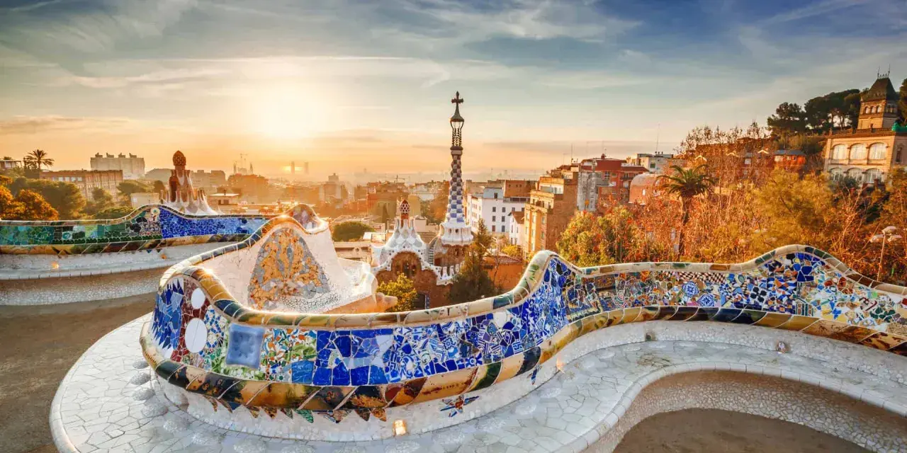 Bancos de mosaico coloridos en el Park Güell, un lugar imprescindible que ver en Barcelona, con la ciudad al amanecer.