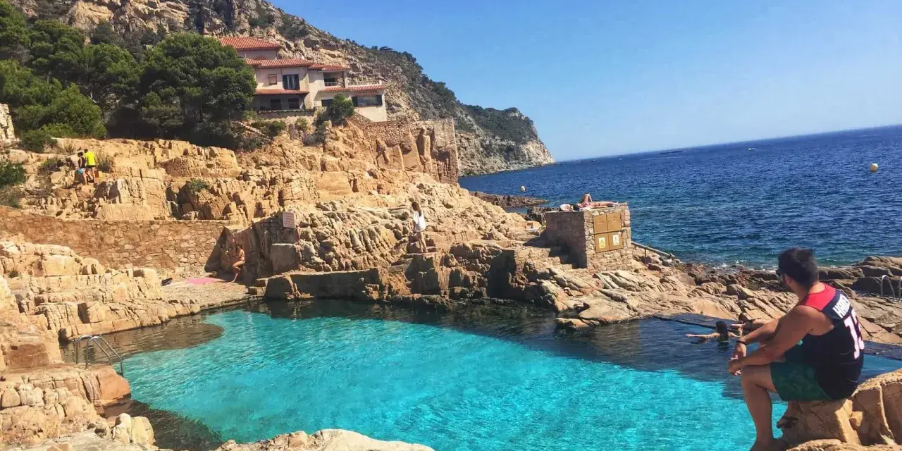 Piscinas naturales de Begur, con aguas cristalinas y rocas doradas. Un hombre contempla el mar azul.