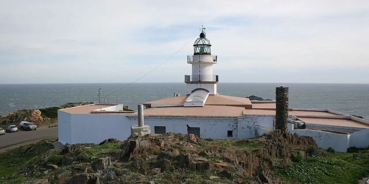 El faro de Cap de Creus se alza blanco y firme sobre rocas escarpadas, vigilando el mar azul.
