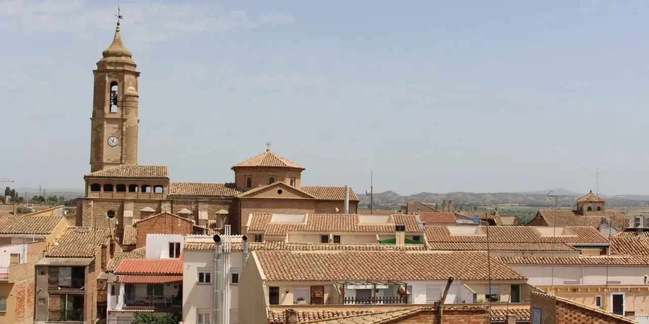 Vista aérea de un pueblo con tejados de teja, destacando una torre de iglesia con reloj. Hay mucho que ver en este pintoresco lugar.