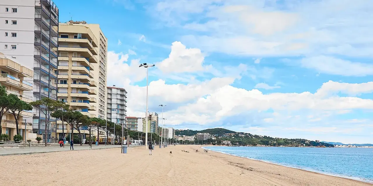 Amplia playa de arena dorada en la playa de Aro centro, con edificios altos a la izquierda y el mar azul a la derecha.