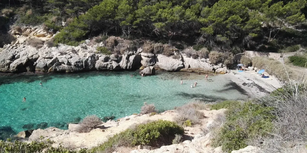 Es caló de la bella dona, una cala escondida con aguas turquesas y rocas escarpadas, donde algunos bañistas disfrutan del sol y el mar.
