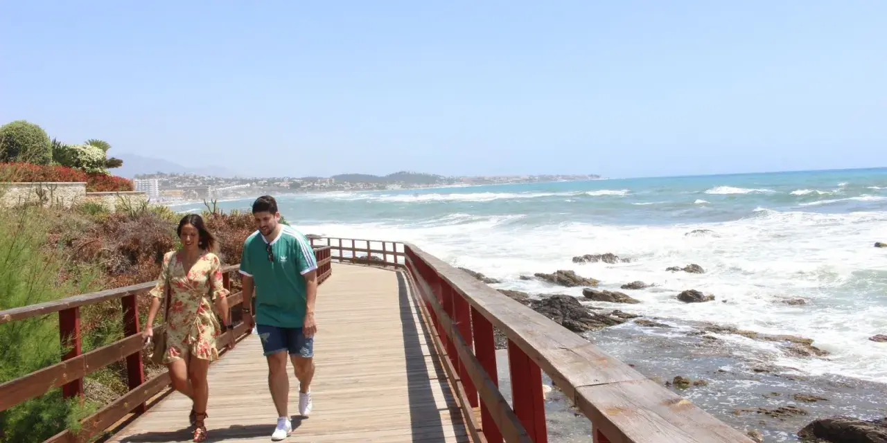 Pareja paseando por un sendero de madera con vistas al mar y la costa de Mijas. ¡Un lugar ideal que ver en Mijas Costa!