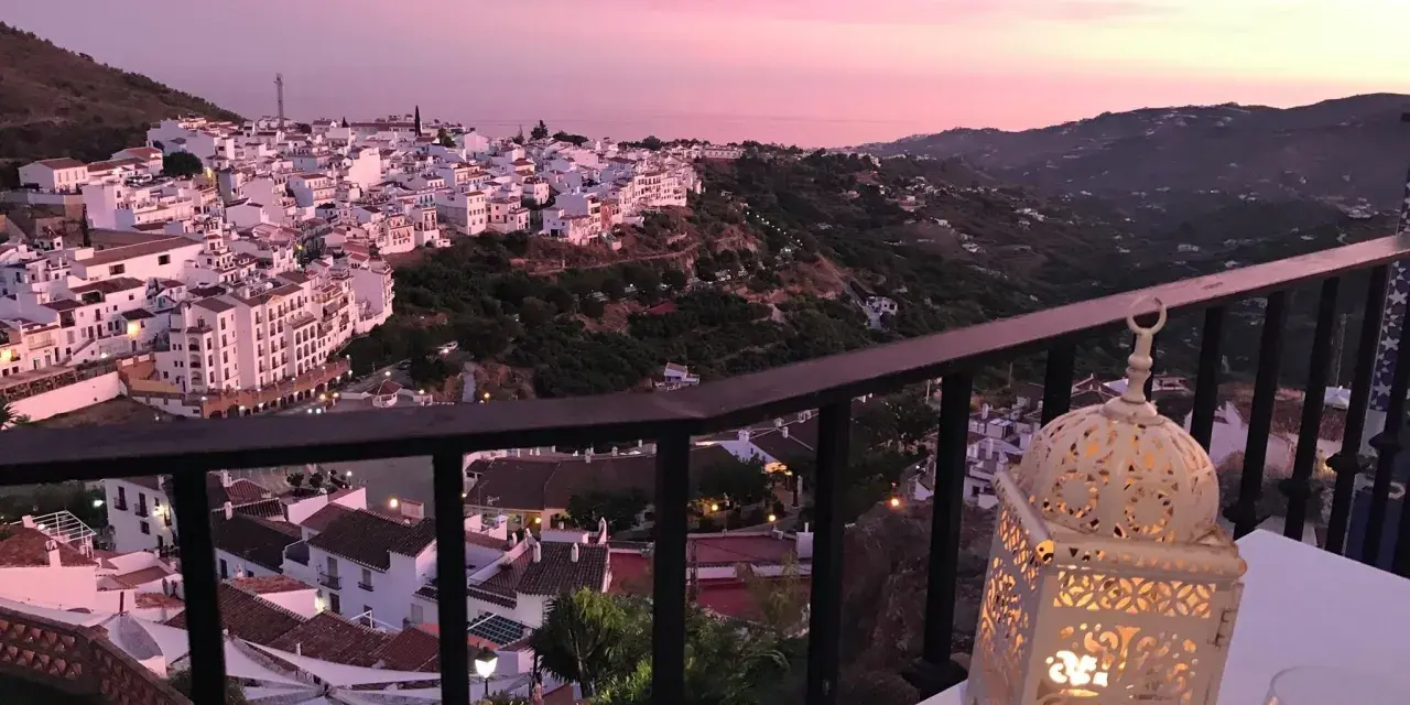 Atardecer rosado sobre Frigiliana. Una linterna ilumina la mesa, perfecta para decidir dónde comer en Frigiliana.