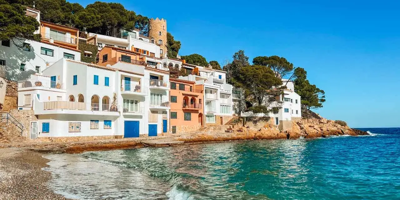Pueblo blanco en la costa, ideal para tu guía Costa Brava. Casas blancas y naranjas con vistas al mar turquesa.