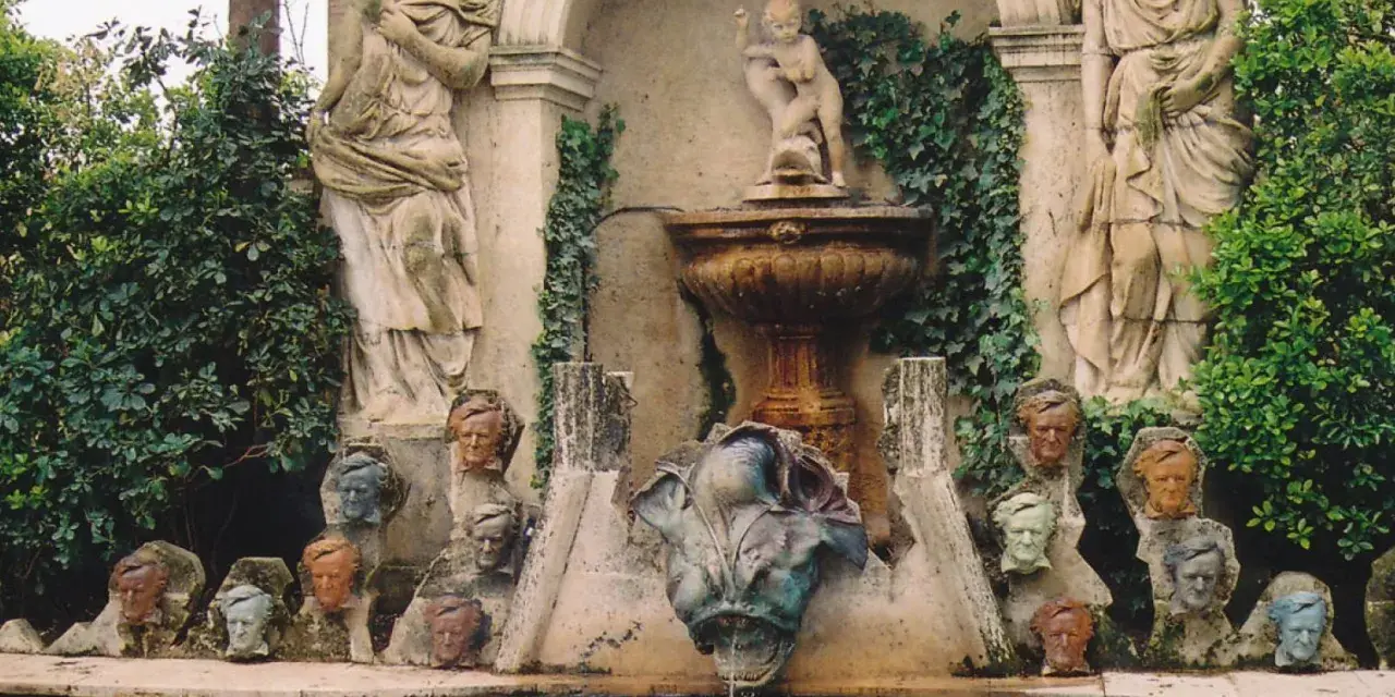 Fuente con estatuas y cabezas de piedra, evocando un antiguo castillo de gala.