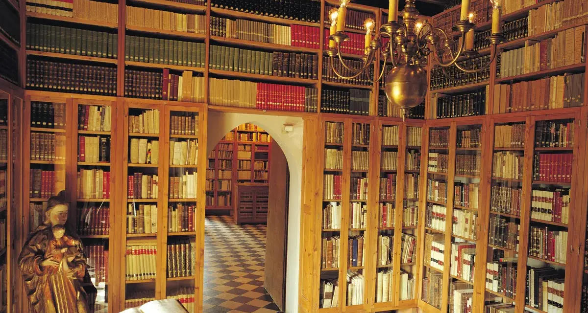 Interior del museu del castell de Peralada, con estanterías repletas de libros antiguos y una lámpara de araña dorada.