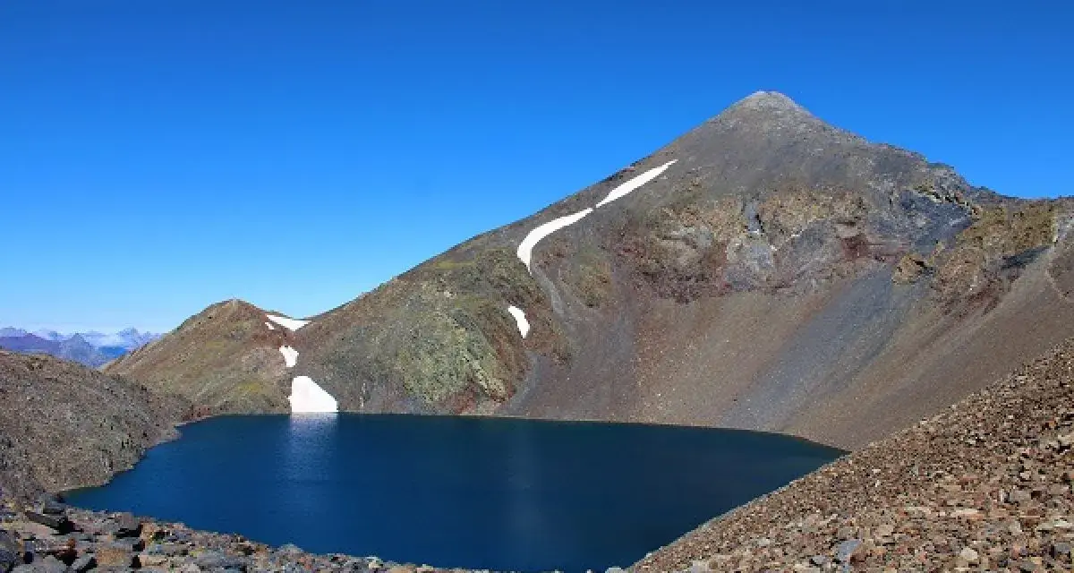 Lago azul profundo en el collado de Tebarray, rodeado de montañas rocosas y con restos de nieve.