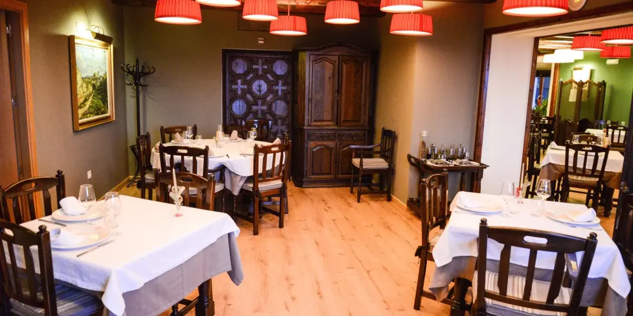 Mesas puestas y listas para comer en Morella. El restaurante tiene lámparas rojas, muebles de madera oscura y un cuadro en la pared.