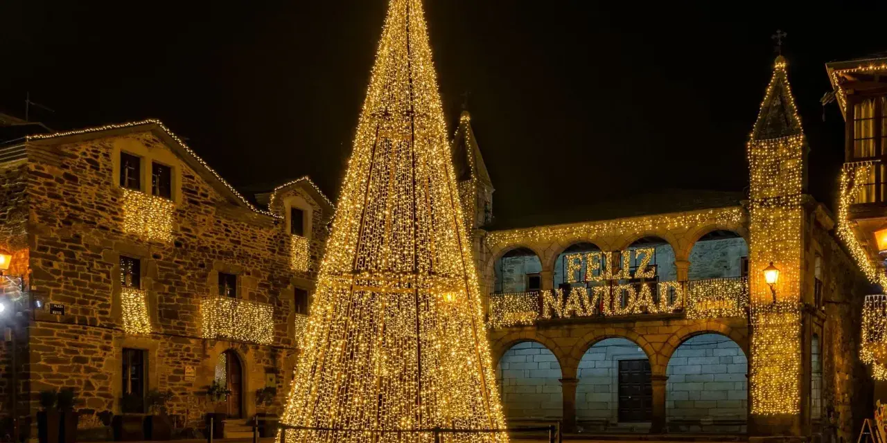 Árbol de Navidad gigante iluminado en una plaza, con edificios adornados y el mensaje "Feliz Navidad". Un lugar ideal que visitar en Navidad en España.