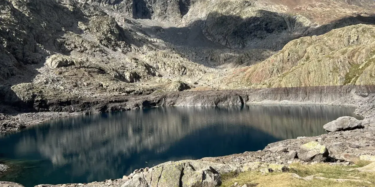 Un lago de montaña de aguas azules profundas, reflejando las cumbres rocosas y el cielo. Un paisaje perfecto para la ruta ibones azules.