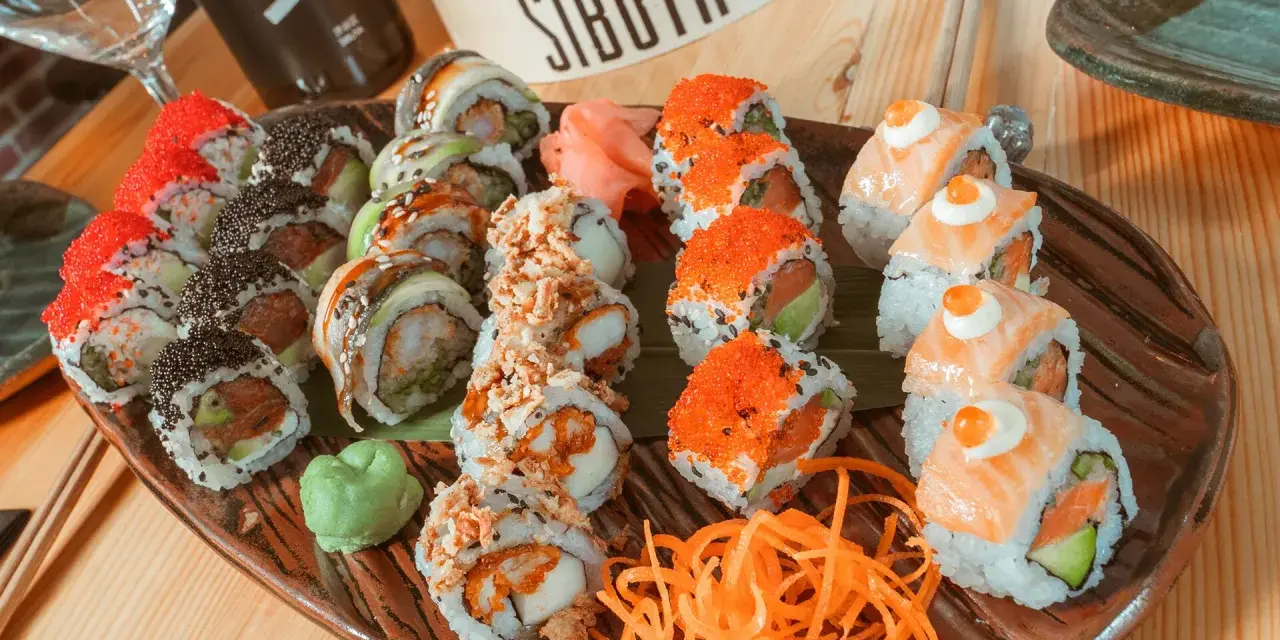 Variedad de sushi en plato marrón, ideal para saber donde comer en Vitoria. Incluye rollos con salmón, huevas de pez volador, aguacate y tempura.