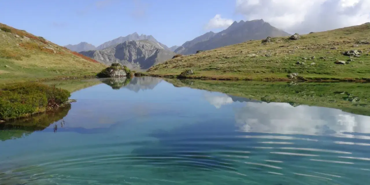 Un sereno ibón de espelunciecha refleja montañas y cielo azul.