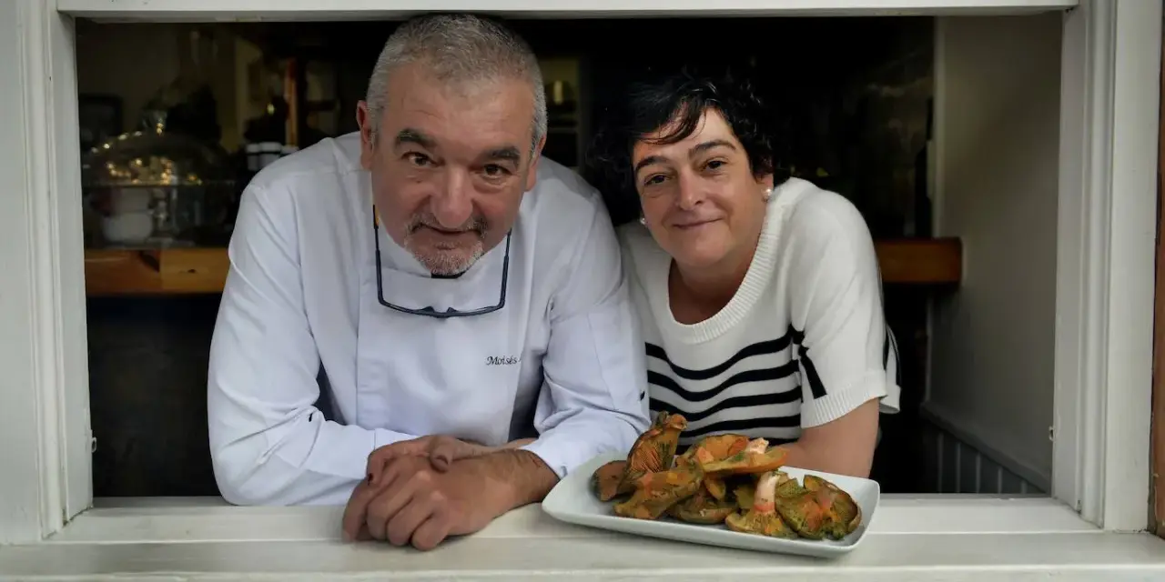 Chef y camarera sonríen tras ventana con plato de setas. Descubre dónde comer en Castro Urdiales.