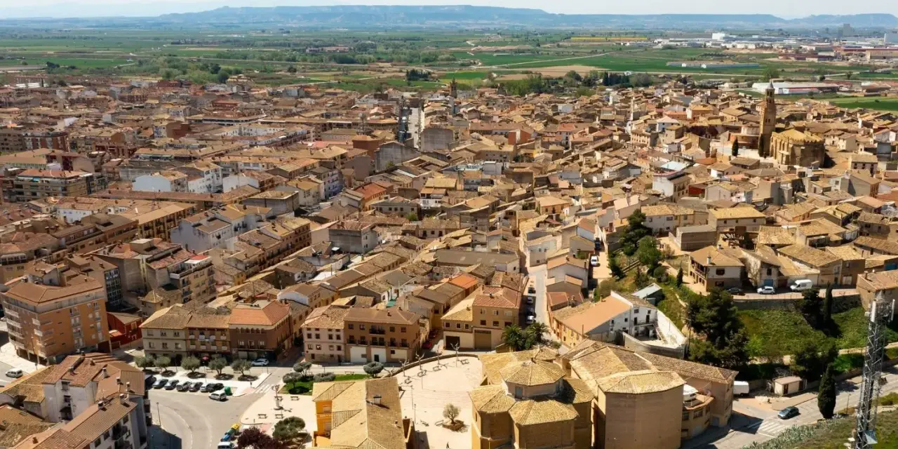 Vista aérea de un pueblo español con tejados de teja, donde se alza la torre de una iglesia. La **ejea de los caballeros** se extiende hasta el horizonte.