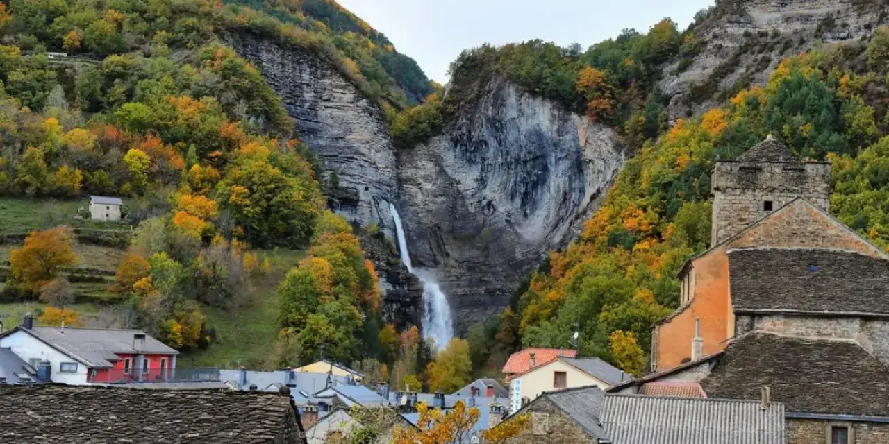 Cascada espectacular en Broto, Huesca, rodeada de bosques otoñales y casas de piedra.