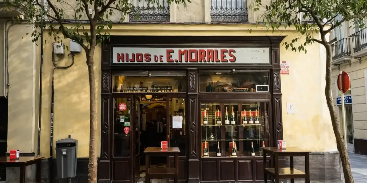 Fachada de "Hijos de E. Morales", un bar tradicional en Sevilla, con mesas en la acera y botellas expuestas.