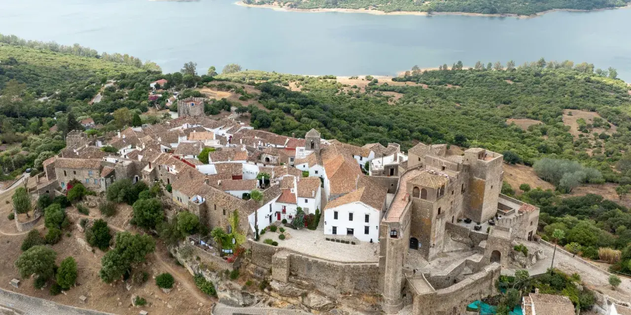 Vista aérea de Castellar de la Frontera, un pueblo blanco con un castillo, rodeado de vegetación y un embalse. Un lugar que evoca la paz de los hippies.
