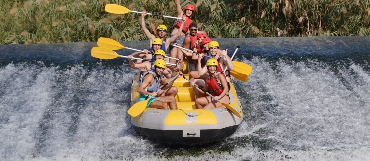 Un grupo de personas disfruta del rafting, remando con entusiasmo en una balsa amarilla sobre aguas turbulentas. ¡Una aventura emocionante!