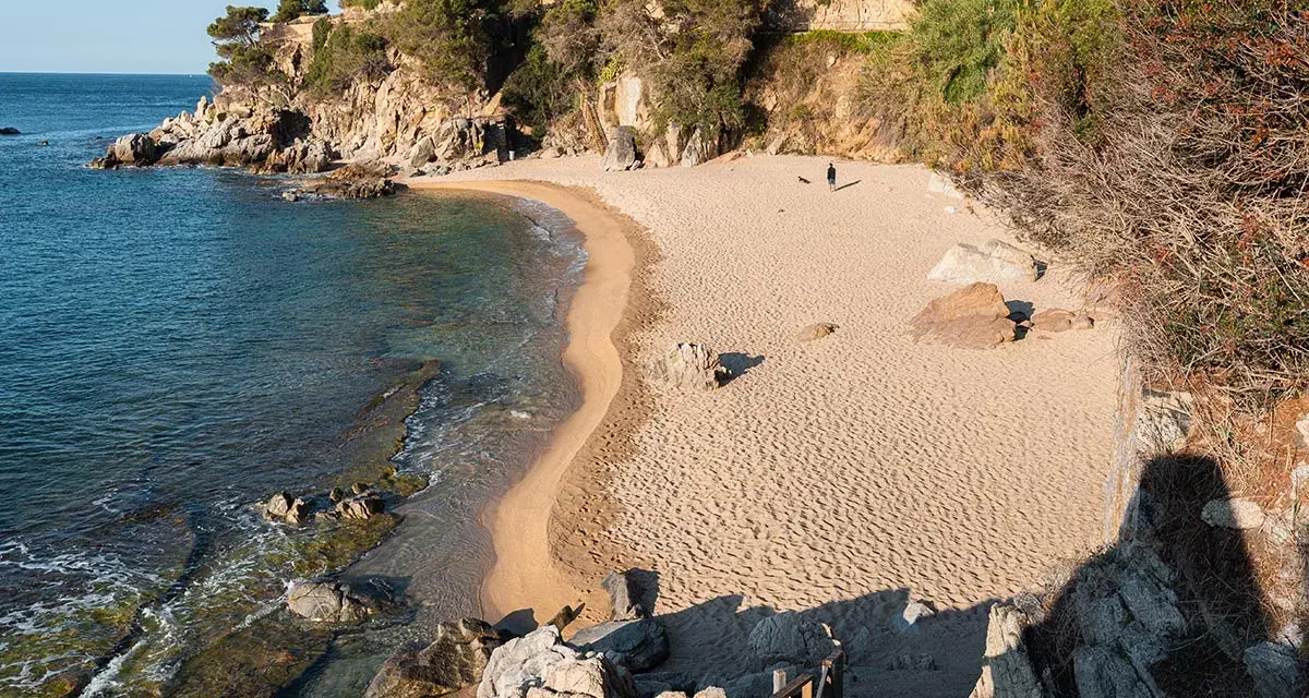 Una persona pasea por la cala belladona, con arena dorada y aguas cristalinas.