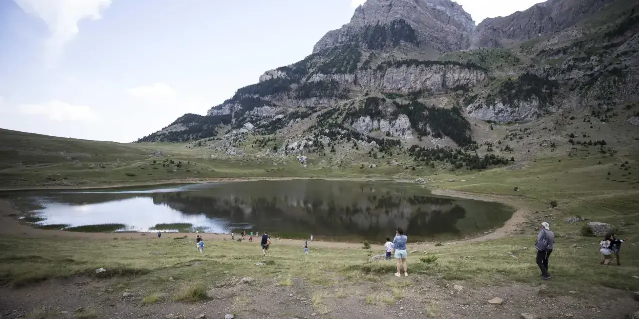 Gente paseando cerca de un lago en el valle de Tena, ideal para rutas de senderismo. Montañas escarpadas al fondo.