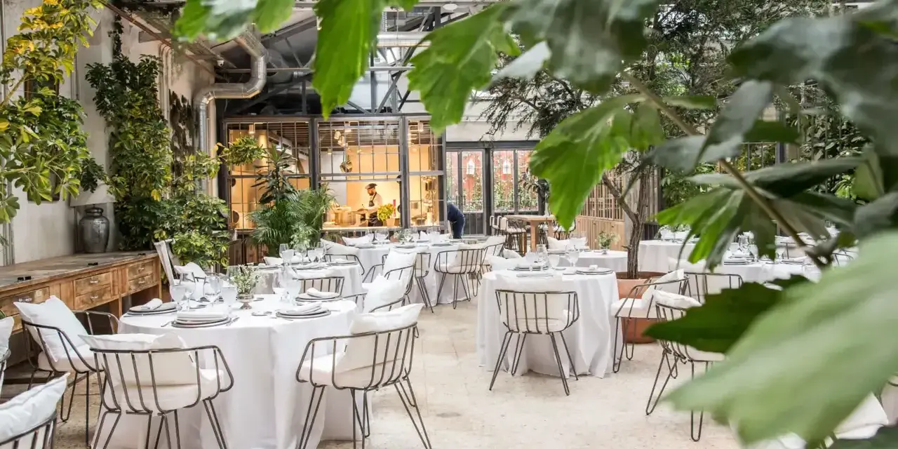 Mesas elegantemente puestas en un invernadero con vegetación exuberante. Un lugar ideal para saber donde comer en Madrid.