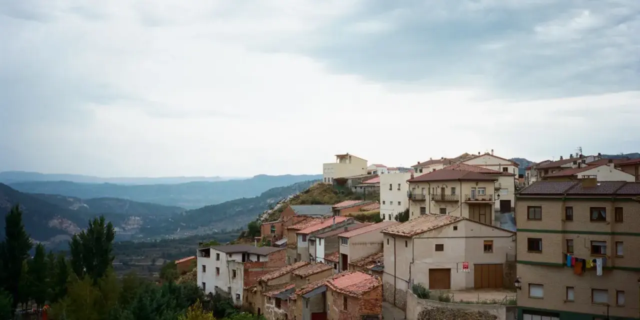 Pueblo español en ladera, con casas de tejados rojos y vistas a montañas. Se ven más de las matas verdes que rodean el asentamiento.