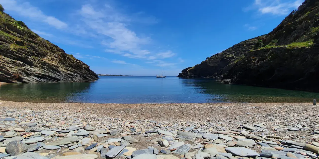 Cala Sa Sabolla, una bahía rocosa con aguas cristalinas y un velero solitario.