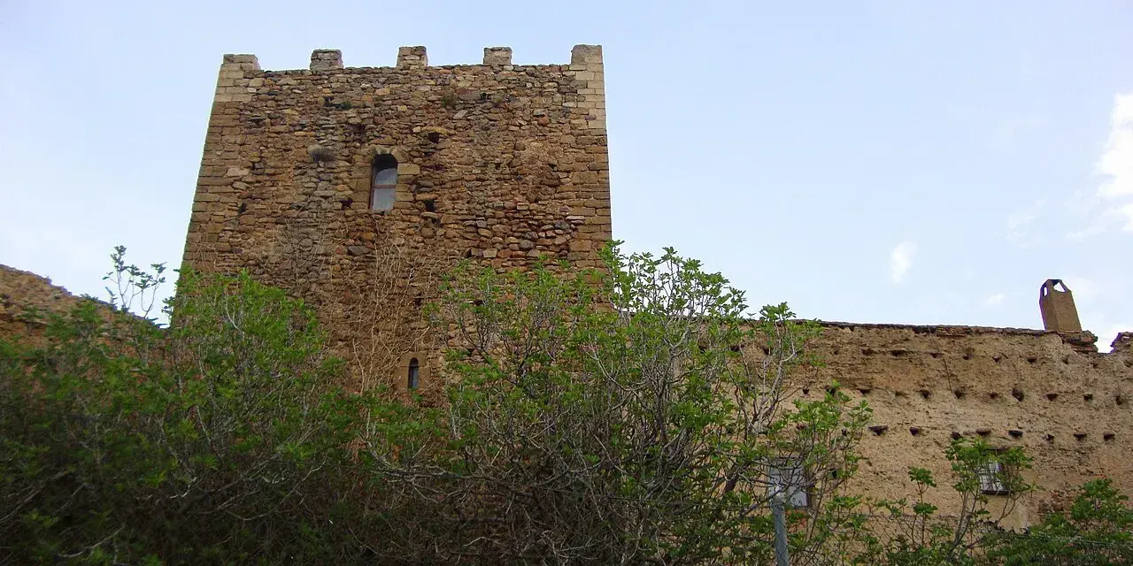 Castillo de piedra con almenas y vegetación frondosa delante.