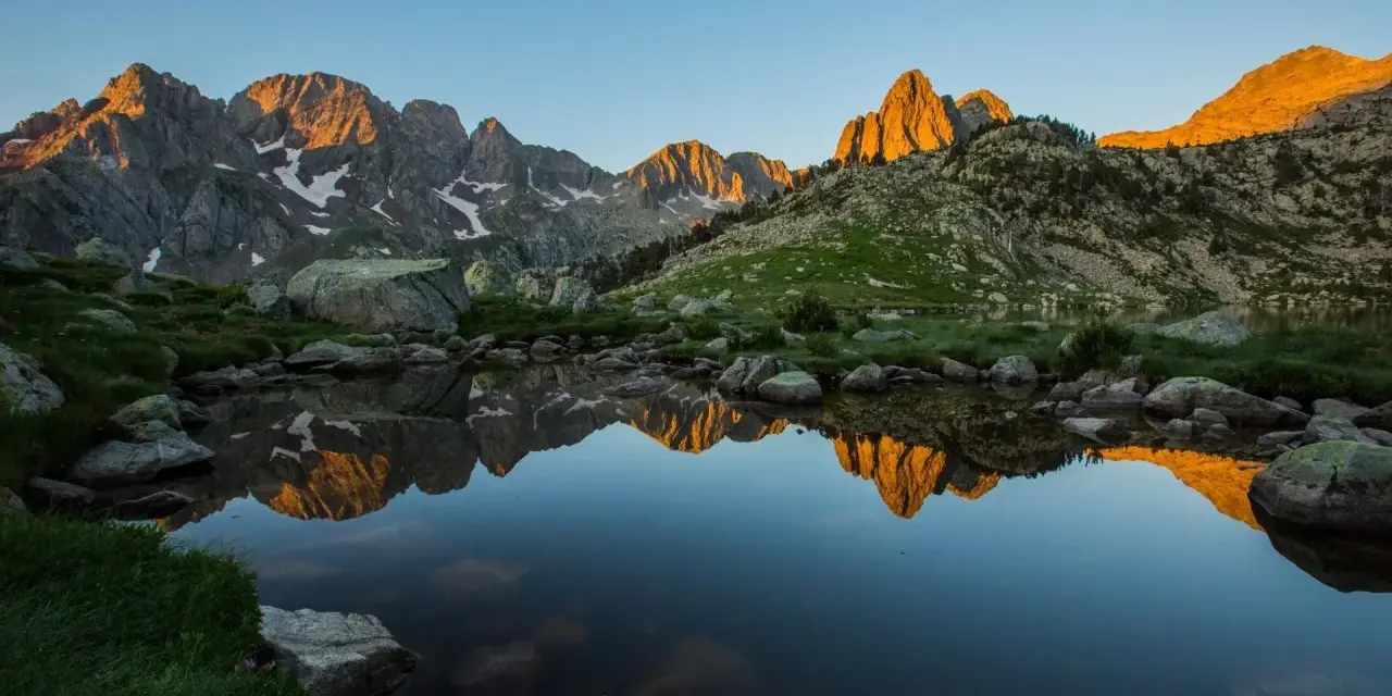 Reflejo dorado de montañas en un lago sereno del **parque natural Posets Maladeta** al amanecer.
