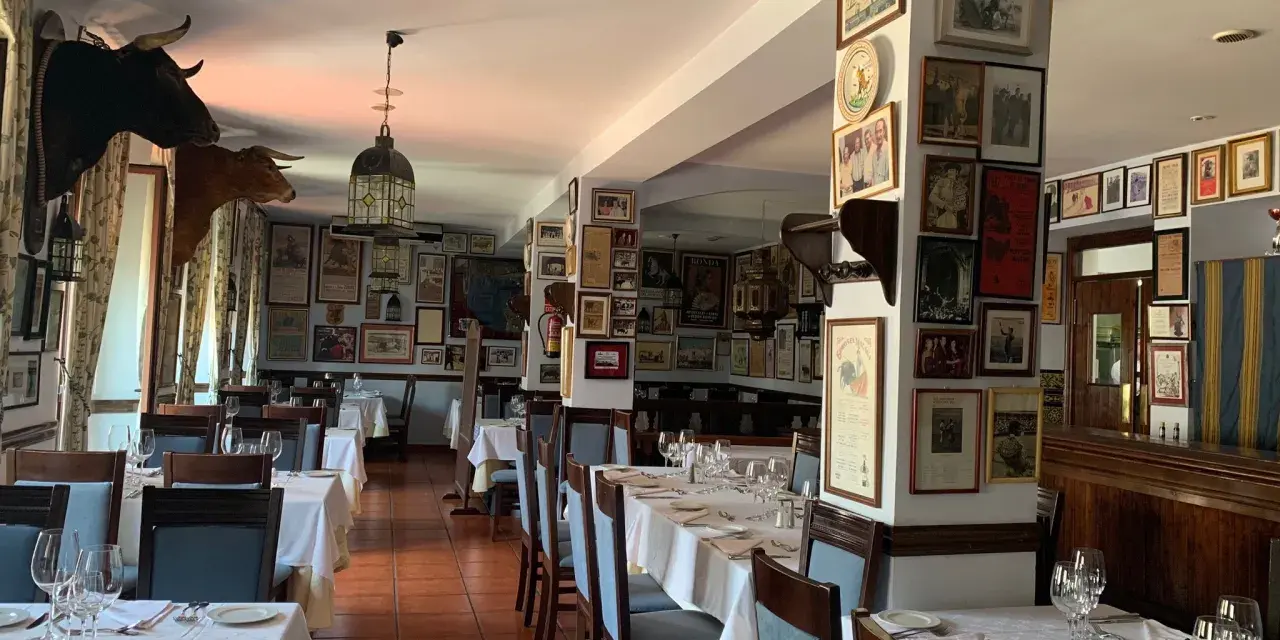 Mesas puestas para comer en ronda, decorado con cabezas de toro y carteles taurinos.
