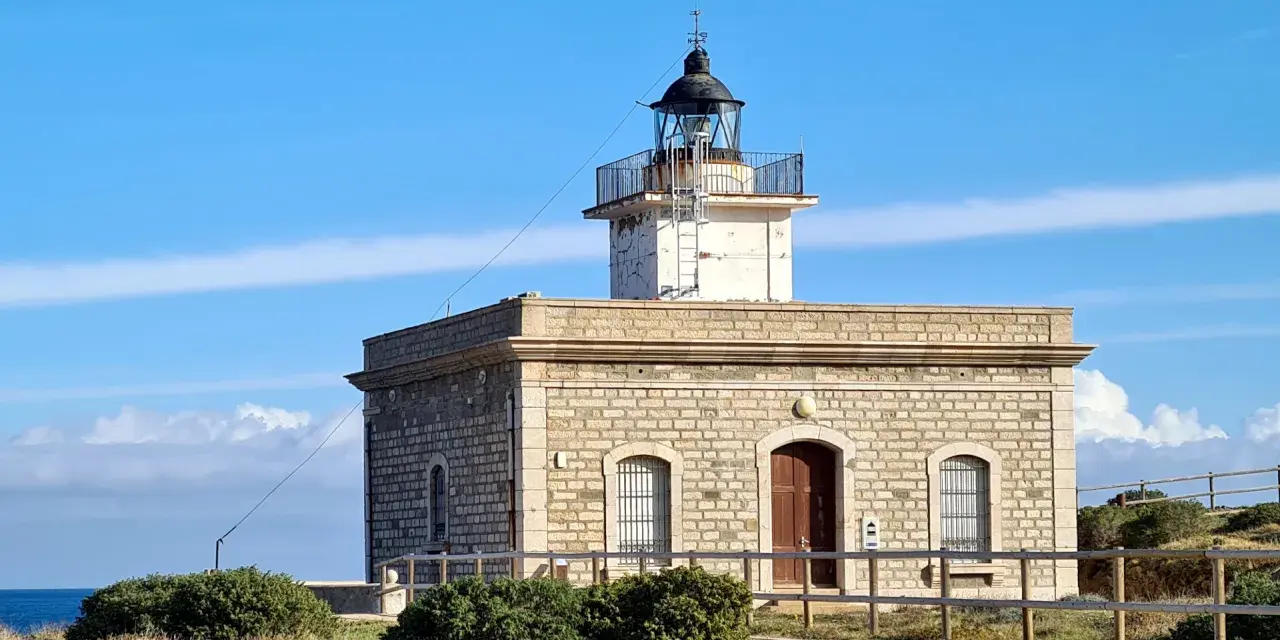 Faro de piedra con torre blanca y cúpula negra, vigilando el mar azul cerca del far port de la selva.