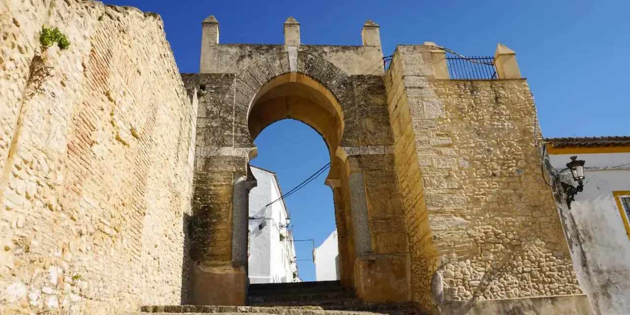 Antigua puerta de Medina Sidonia, con escalinata de piedra y cielo azul. Merece la pena visitar Medina Sidonia.