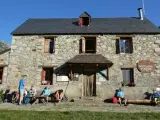 Grupo de excursionistas descansa frente al Refugio Viados, parte de la ruta de los tres refugios. Montañas y cielo azul al fondo.