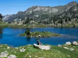 Persona sentada en roca contempla los lagos de Colomers en una ruta corta. Paisaje montañoso y azul intenso.