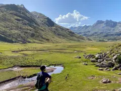 Un excursionista contempla un vasto valle de hecho, con un río serpenteante y montañas majestuosas bajo un cielo azul.