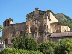 El **monasterio de Siresa**, con su imponente arquitectura de piedra y campanario, se alza bajo un cielo azul, rodeado de vegetación exuberante.