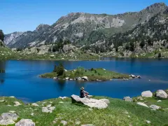 Persona sentada en roca contempla los lagos de Colomers en una ruta corta. Paisaje montañoso y azul intenso.