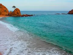 La platja mar menuda, con sus rocas anaranjadas y aguas turquesas, invita a soñar. Una ola rompe suavemente en la arena dorada.