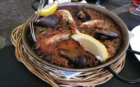 Paella marinera con gambas y mejillones, un plato típico de los restaurantes de Blanes, servida en una paellera sobre una cesta de mimbre.