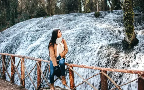 Joven admira la cascada en el Monasterio de Piedra, Zaragoza. El agua cae en cascada sobre rocas cubiertas de musgo, creando un paisaje natural impresionante.