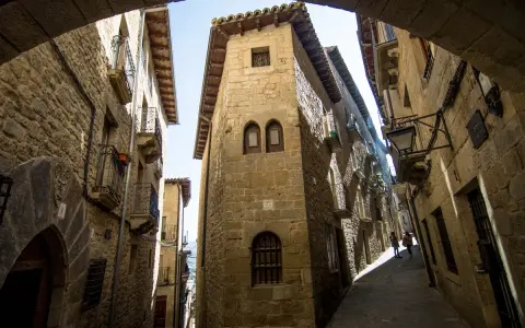 Calle empedrada con edificios de piedra, balcones de hierro y un arco. Un lugar que evoca la historia de los Reyes Católicos.