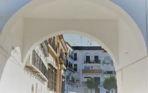 Un arco blanco enmarca edificios blancos y ocres con balcones de hierro forjado. Descubre qué ver en Marchena, un rincón andaluz lleno de encanto.