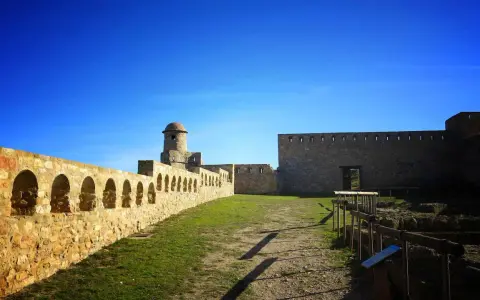 Impresionante castillo de piedra con murallas, arcos y torreón. Un lugar histórico que ver en Benabarre, bajo un cielo azul intenso.