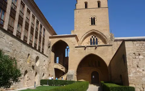 El **castillo de Alcañiz**, con su imponente torre y arcos, se alza bajo un cielo azul. Jardines cuidados y muros de piedra evocan su historia.