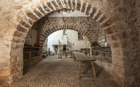 Interior de la torre de las arcas, con arcos de piedra, estanterías rústicas y un horno antiguo.