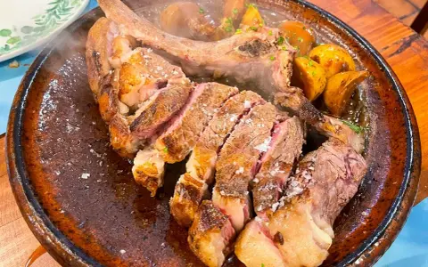Un jugoso chuletón a la brasa, cortado y servido con patatas asadas, perfecto para comer en Tui.