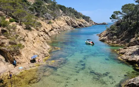 Una cala idílica en Tossa de Mar con aguas cristalinas, rocas escarpadas y un pequeño bote.