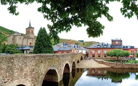 Puente romano y el pueblo de Molina Seca que ver. Iglesia antigua, casas y río con reflejos.
